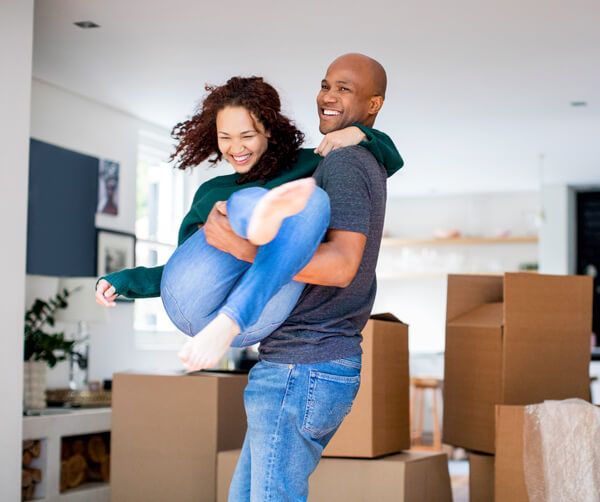 First time home buyer tips. Man carries his wife past moving boxes and into their new home.