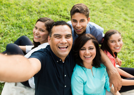 Latino family smiling and posing for portrait together on green lawn