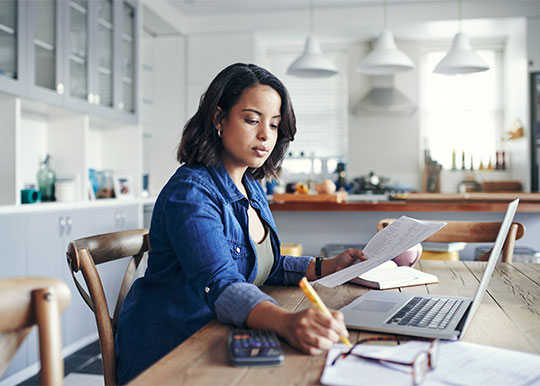 young woman using a laptop and going through paperwork while working from home