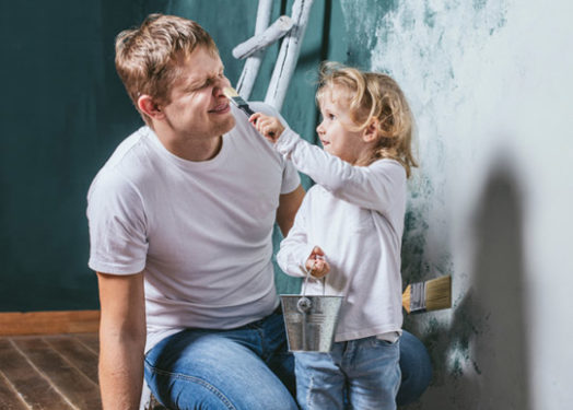Un padre feliz y su hija pequeña comparten un momento divertido mientras pintan una habitación.