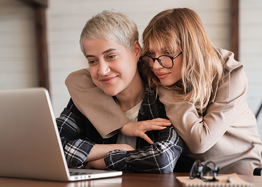 two women embraced looking at laptop